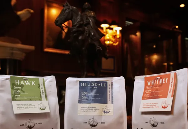 Three bags of Ad Astra coffee — Hawk, Hillsdale Blend and Whitney — in a wood-paneled room